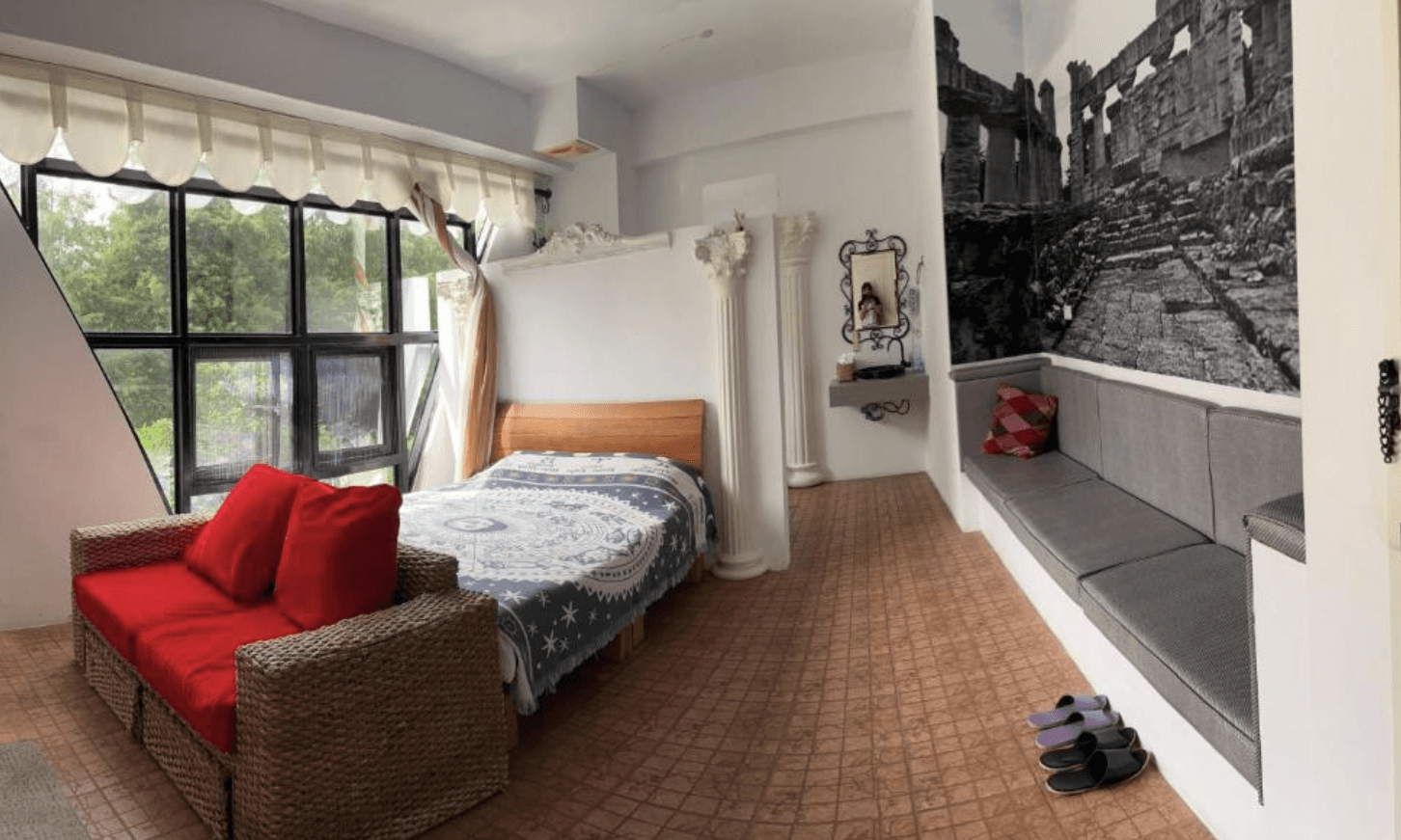 【三義住宿】慕哲哈比屋的希臘風格主題房型，設有羅馬柱裝飾與黑白古蹟壁畫，藤編沙發配上鮮紅抱枕，窗邊採光良好，空間富有異國情調。