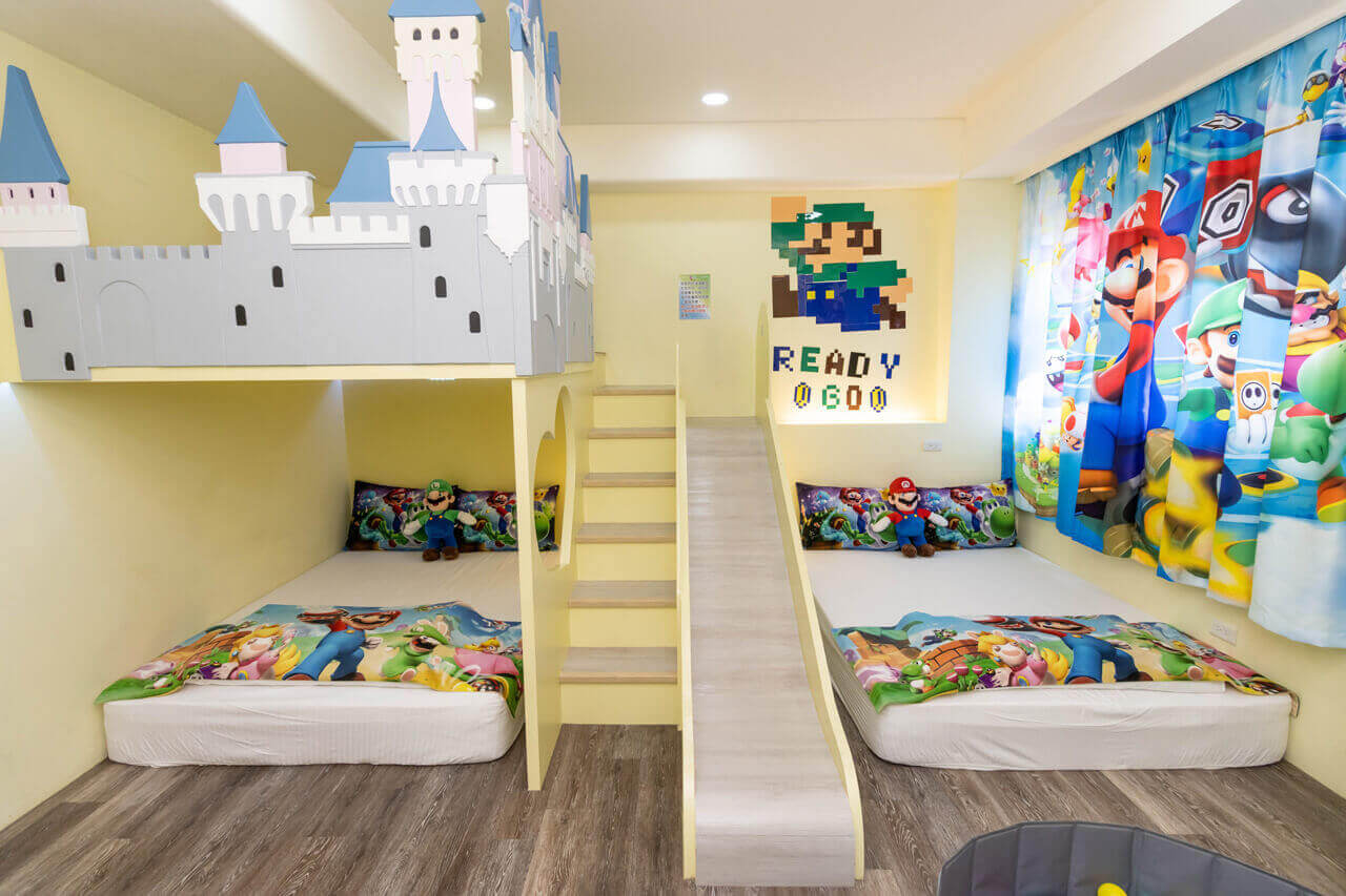 【五結住宿】掬月童心親子民宿以超級瑪利歐為主題的親子房型，設有兩張地板床與滑梯、城堡造型上下舖，牆面與窗簾皆為遊戲角色裝飾，充滿童趣與色彩。
