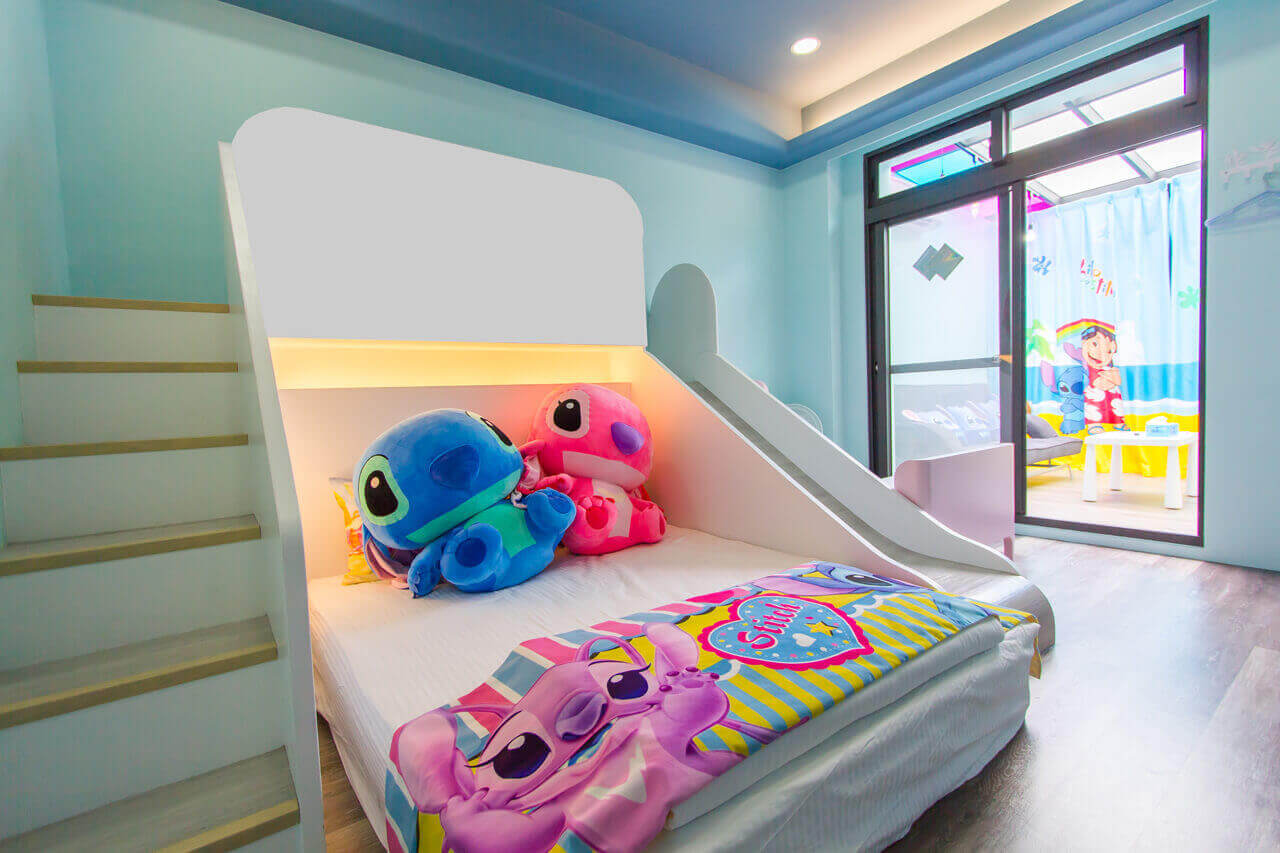 【五結住宿】掬月童心親子民宿的史迪奇主題親子房，設有滑梯與上下舖，床上擺有大型史迪奇與天使玩偶，整體以清爽藍色為主，窗簾上有夏日海灘圖樣。