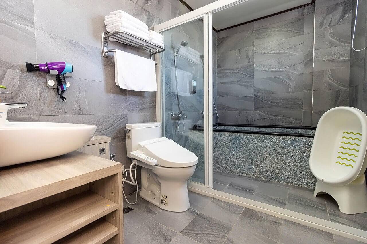 【五結住宿】掬月童心親子民宿的親子衛浴空間，配有免治馬桶、乾濕分離淋浴間、浴缸及兒童澡盆，牆面為灰色石紋磁磚設計，整潔舒適。