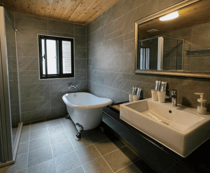 【東港住宿】東帆巷弄休閒民宿的灰色磁磚牆面搭配木質天花板，設有復古獨立浴缸、大型鏡面與長形洗手台，空間寬敞、氛圍高雅，提供舒適的泡澡體驗。