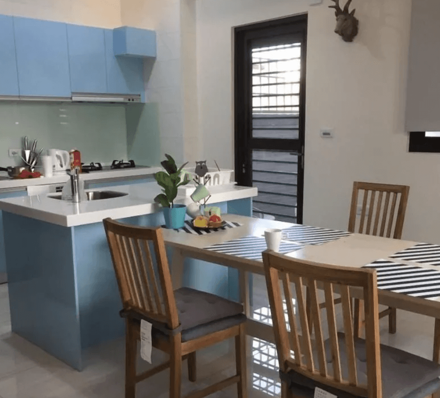 【東港住宿】東帆巷弄休閒民宿的廚房採用淺藍與白色系設計，配有中島、瓦斯爐、水槽與多種廚具，旁邊設有木質四人餐桌，風格清新簡約，適合家庭旅遊或長住使用。