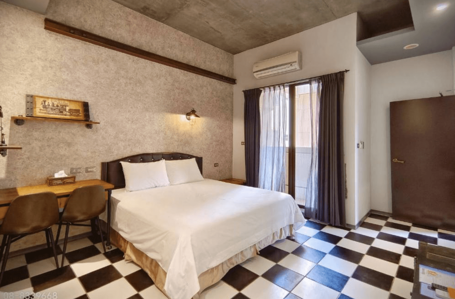 【東港住宿】東港幸福168民宿以灰牆與水泥天花板結合黑白格地磚設計，房內設有一張雙人床與復古風雙人書桌，床頭牆面懸掛工業風燈具與裝飾畫，風格獨特有個性。