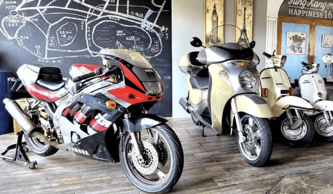 【東港住宿】東港幸福168民宿的大廳展示多台復古重機與速克達，牆面畫有手繪地圖與歐式裝飾，木質地板與古典元素交織出濃厚的文青風格，吸引喜愛摩托車文化的旅人。