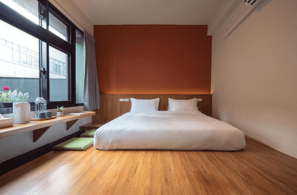 【彰化飯店】東皋歇暝和風雙人房，設有低床台雙人床與木地板，窗邊配置茶具與坐墊，牆面以橘色為主體，風格溫暖自然。
