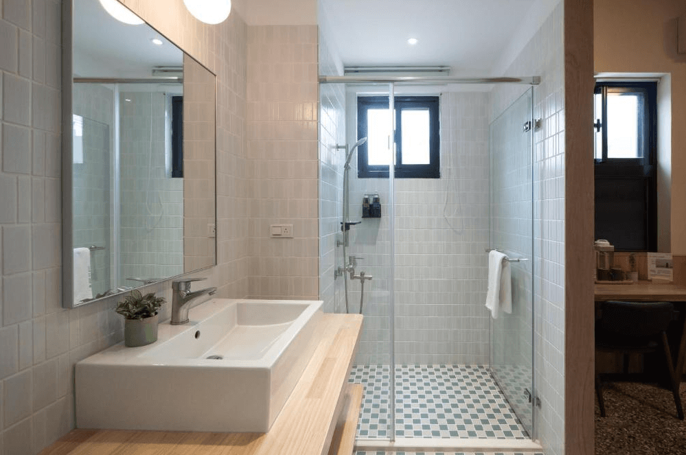 【彰化飯店】東皋歇暝浴室空間，設有大面鏡與長型洗手台，乾濕分離淋浴間以玻璃隔間，磁磚風格清新雅緻。