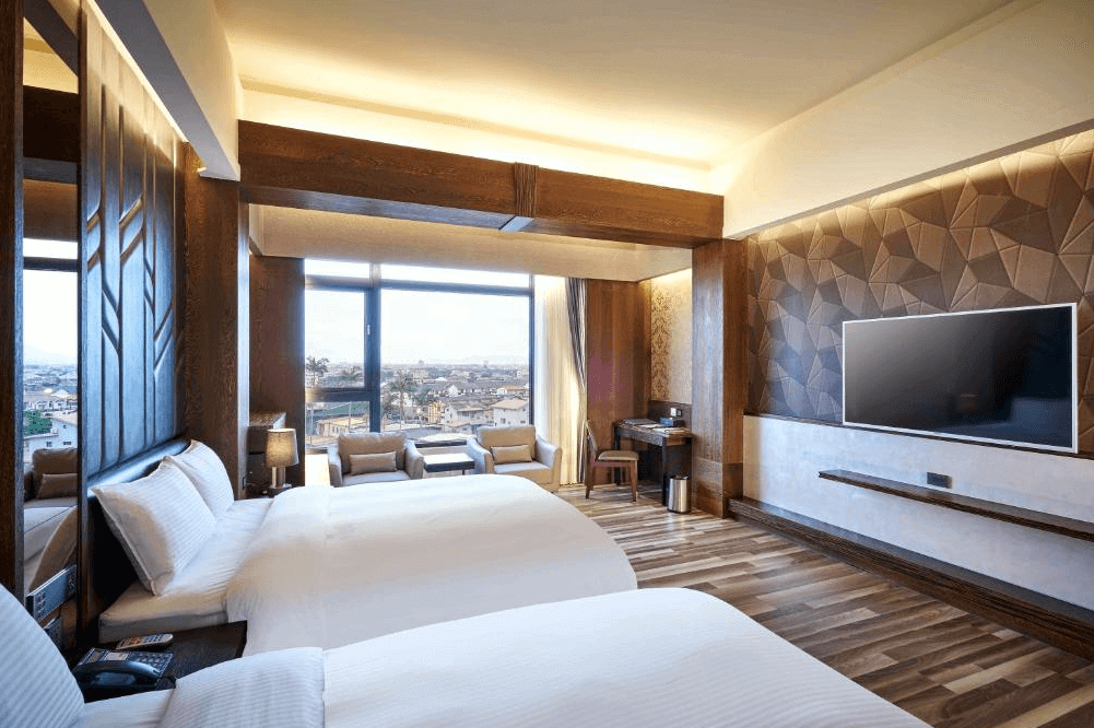 【五結住宿】松風文旅的雙床客房，搭配幾何木紋牆面與大型平面電視，設有大片落地窗與沙發休憩區，空間寬敞明亮，俯瞰市景視野極佳。