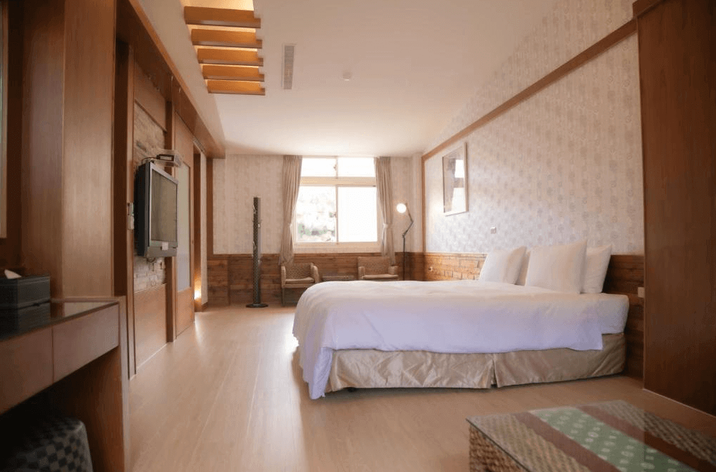 【關子嶺溫泉】“白河住宿”林桂園石泉會館的木質風格景觀套房，配有一張加大雙人床與獨立客廳區域，大面窗戶引進自然光線，營造溫暖舒適的住宿氛圍。