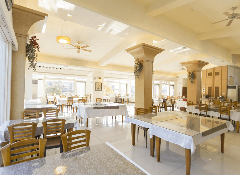 【關子嶺溫泉】“白河住宿”林桂園石泉會館的餐廳空間明亮寬敞，設有多張鋪有白色桌巾的餐桌與木質椅，四周為大面窗景，充滿自然採光。