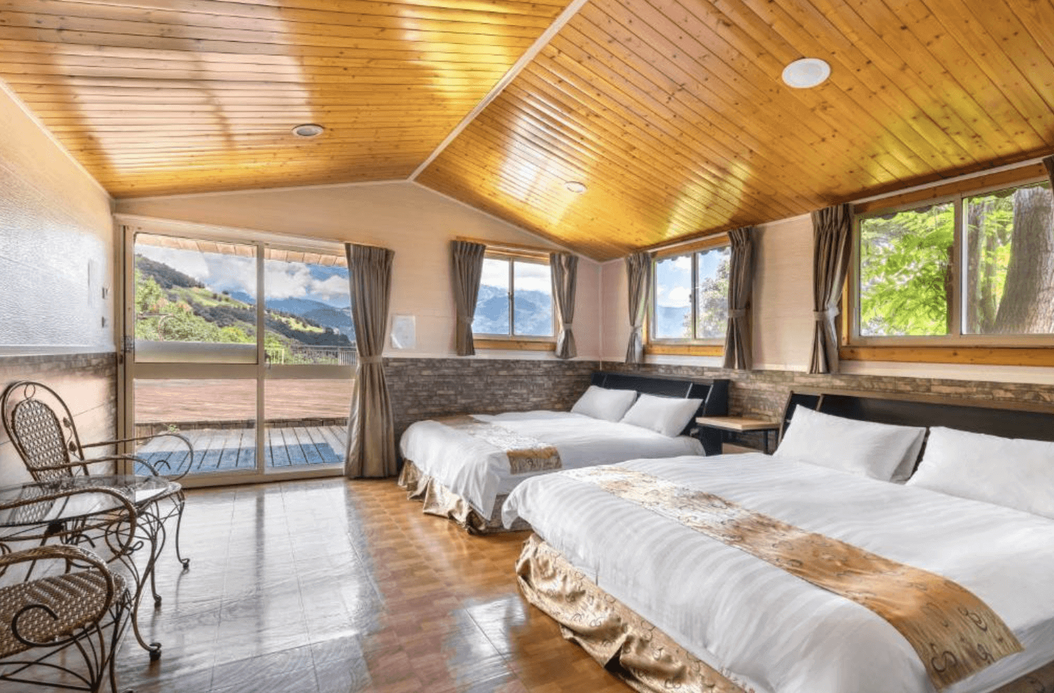 【清境農場住宿】清境之星樂活民宿，擁有木質斜屋頂的四人房，設有兩張大床，房內空間寬敞明亮，大片窗戶與陽台玻璃門帶來充足自然光與遼闊山景，室內設有藤椅座位區，營造溫馨木屋氛圍。
