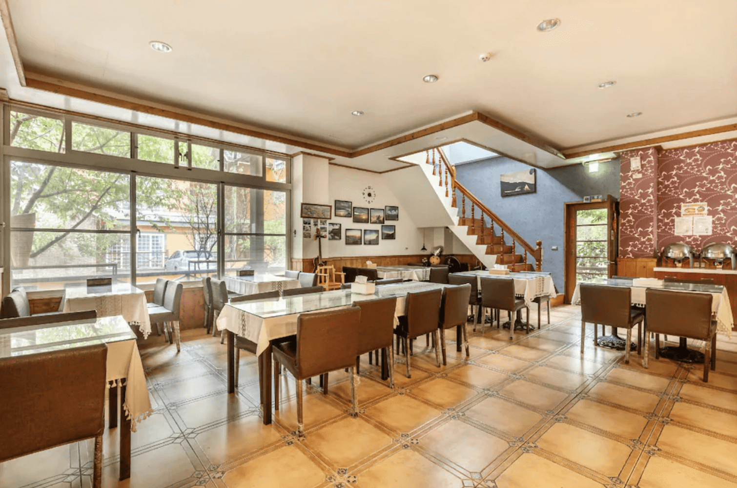 【清境農場住宿】清境之星樂活民宿的室內用餐空間寬敞明亮，大片玻璃窗可眺望戶外綠意。用餐區配置多張方桌與皮革座椅，設有自助餐檯與樓梯通往二樓，牆上裝飾多幅風景攝影作品，營造舒適溫馨的用餐環境。