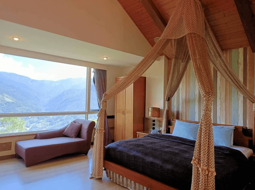 【清境農場住宿】清境夏都夢幻山林渡假山莊，擁有絕美山景的大面落地窗雙人房，房內設有蚊帳裝飾的雙人床與貴妃椅，牆面採木紋與柔和色調，營造出夢幻又寧靜的住宿氛圍。