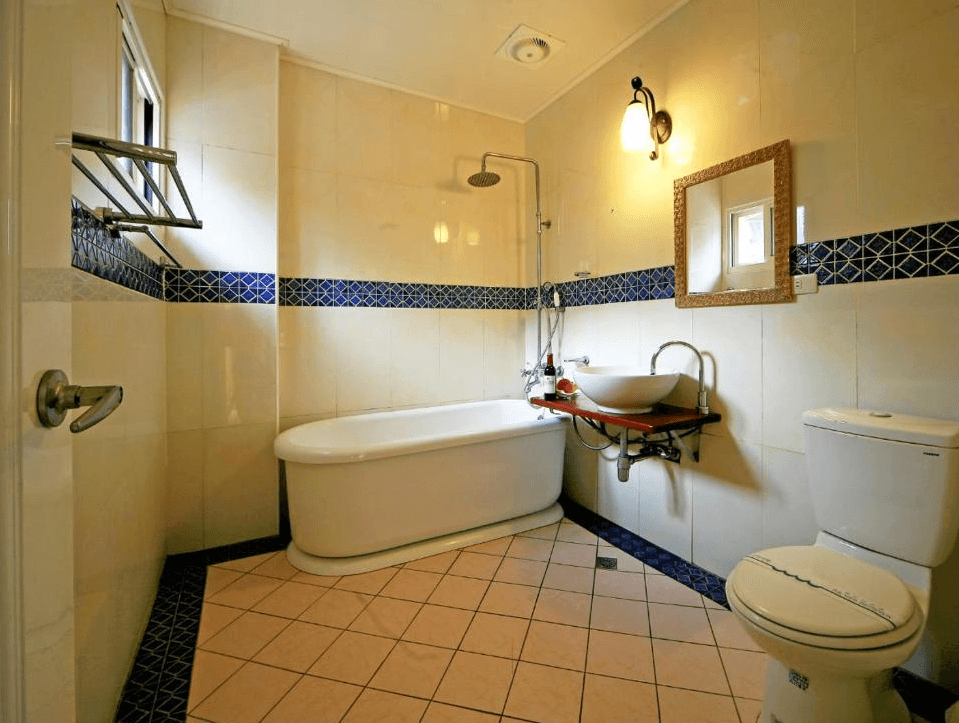 【清境農場住宿】清境夏都夢幻山林渡假山莊的明亮浴室，配有獨立浴缸、蓮蓬頭、造型洗手台與馬桶，牆面以米色與藍色幾何圖案磁磚搭配，呈現出整潔舒適的氛圍。