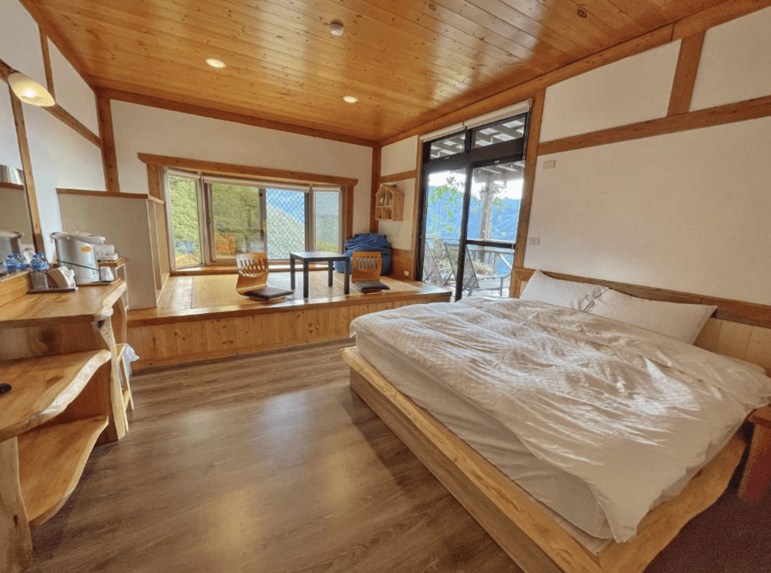 【清境農場住宿】清境天祥景觀民宿的景觀雙人房，配有大床與和式升高地板，設有兩張低椅與茶几可賞景，大片落地窗外即是群山環繞，整體氛圍溫暖舒適，適合放鬆度假。