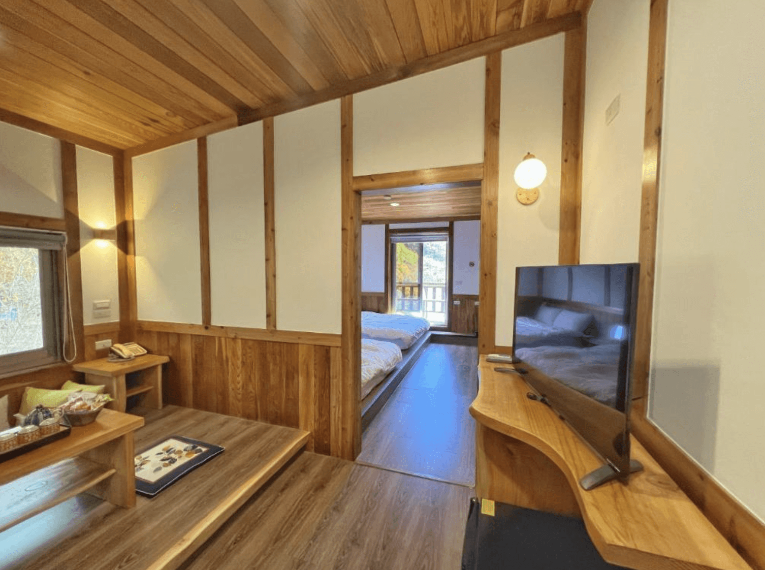 【清境農場住宿】清境天祥景觀民宿以木質設計為主的家庭房空間，前方是日式榻榻米茶敘區，後方通往設有兩張雙人床的臥室空間，電視與基本茶點設施齊全，透過窗戶可欣賞清境山林景致。