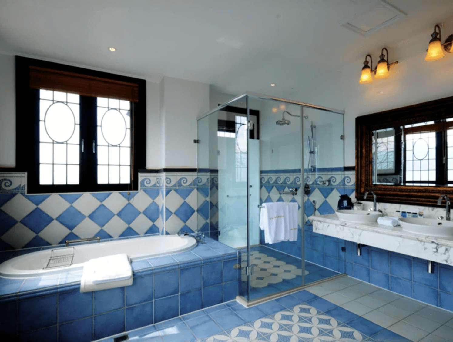 【清境農場住宿】"台灣最貴飯店"清境老英格蘭莊園民宿的浴室空間，以藍白鑽石格紋磁磚打造地板與牆面，設有獨立浴缸、雙人洗手台與乾濕分離玻璃淋浴間，大面窗戶採光極佳，整體明亮清新又典雅。