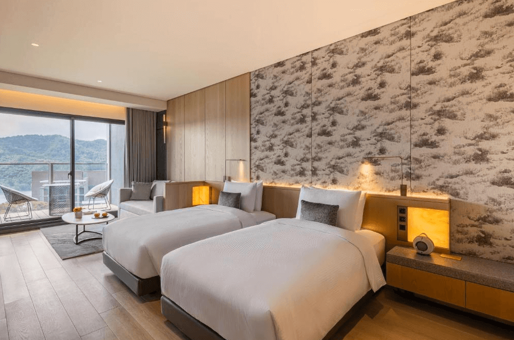 【台灣最貴飯店】漢來日月行館的雙床客房，設有大片落地窗與陽台，可眺望山景，房內採用木質地板與溫暖燈光，牆面為雲霧山嵐圖騰設計，營造出舒適放鬆的住宿氛圍。