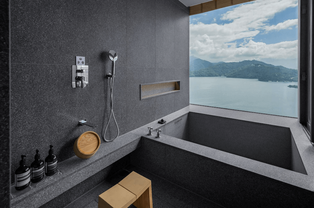 【台灣最貴飯店】漢來日月行館黑灰石材打造的浴室空間，設有景觀大浴缸與淋浴設備，窗外即是壯闊湖景與山巒景致，是享受泡湯與自然美景的絕佳空間。