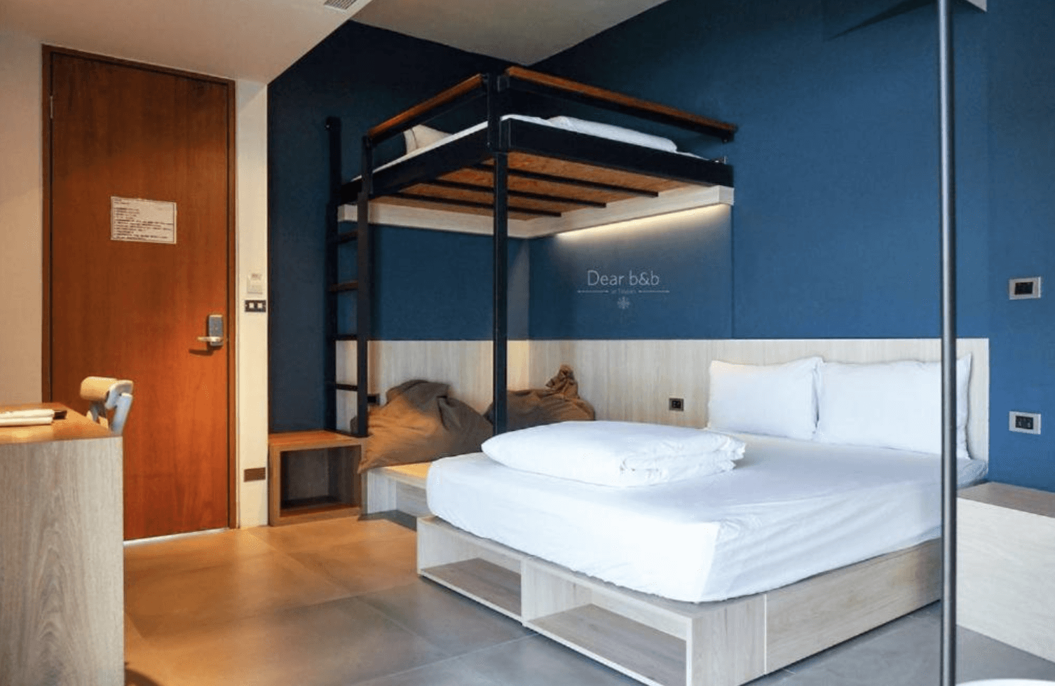 【東港住宿】灣稻旅居的房內設有一張雙人床與一張上舖床架，深藍色牆面與木質元素交織出現代感，房內另有懶人沙發與木質書桌，適合親子或朋友共宿。