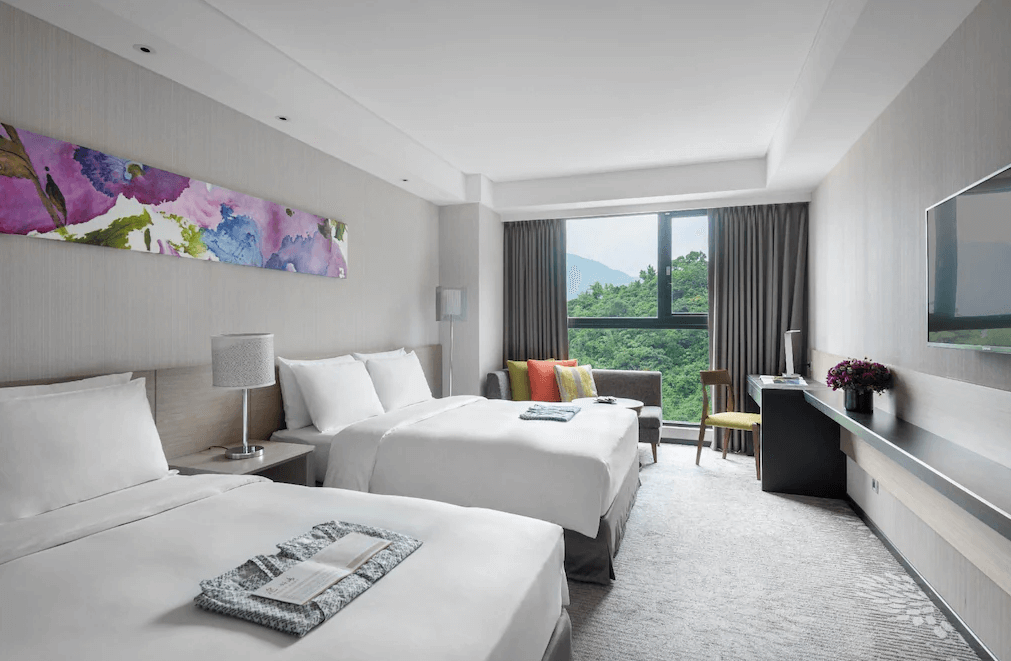 【蘇澳住宿】煙波大飯店蘇澳四季雙泉館的雙人房，設有兩張大床、窗邊沙發及大片景觀窗，可眺望青翠山景，房內採光明亮，牆面掛有色彩繽紛的藝術畫作。