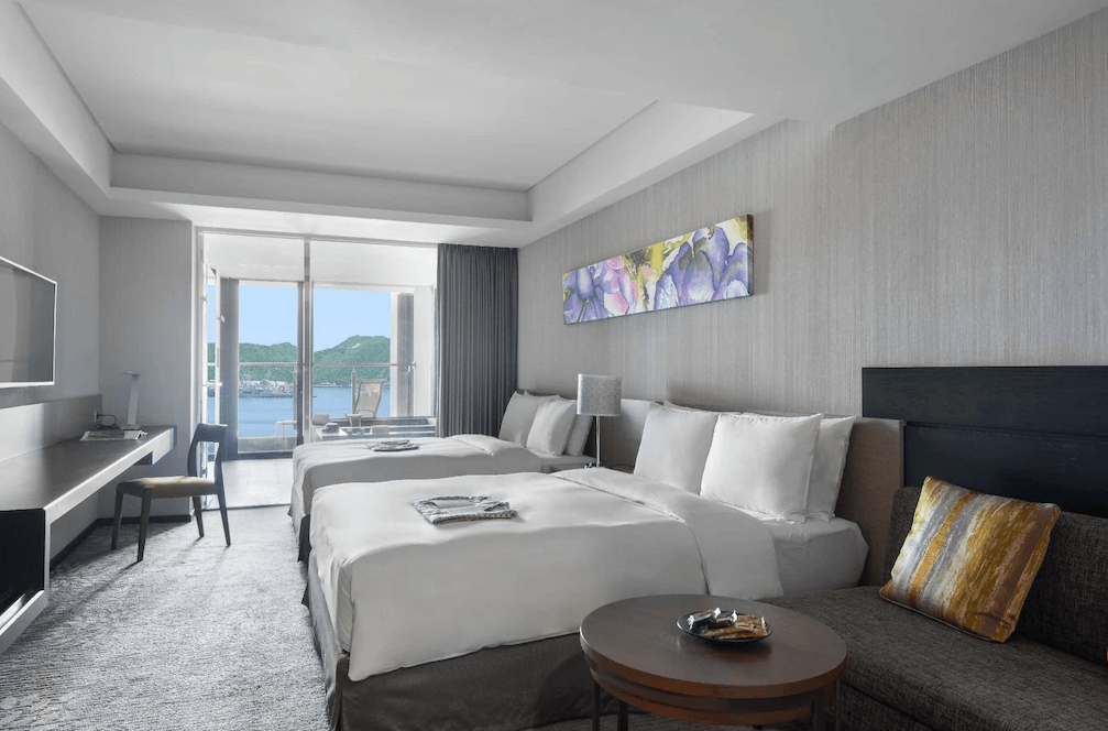 【蘇澳住宿】煙波大飯店蘇澳四季雙泉館的海景家庭房，配有兩張大床與沙發，陽台外可遠眺湛藍海景與綠意山丘，室內擺設簡約溫馨，牆上裝飾鮮豔花卉畫。