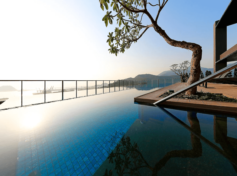 【蘇澳住宿】煙波大飯店蘇澳四季雙泉館的無邊際泳池面向海港，水面與天空交融，夕陽映照出金色光芒，池畔設有造景樹木與木質平台，氣氛靜謐悠閒。