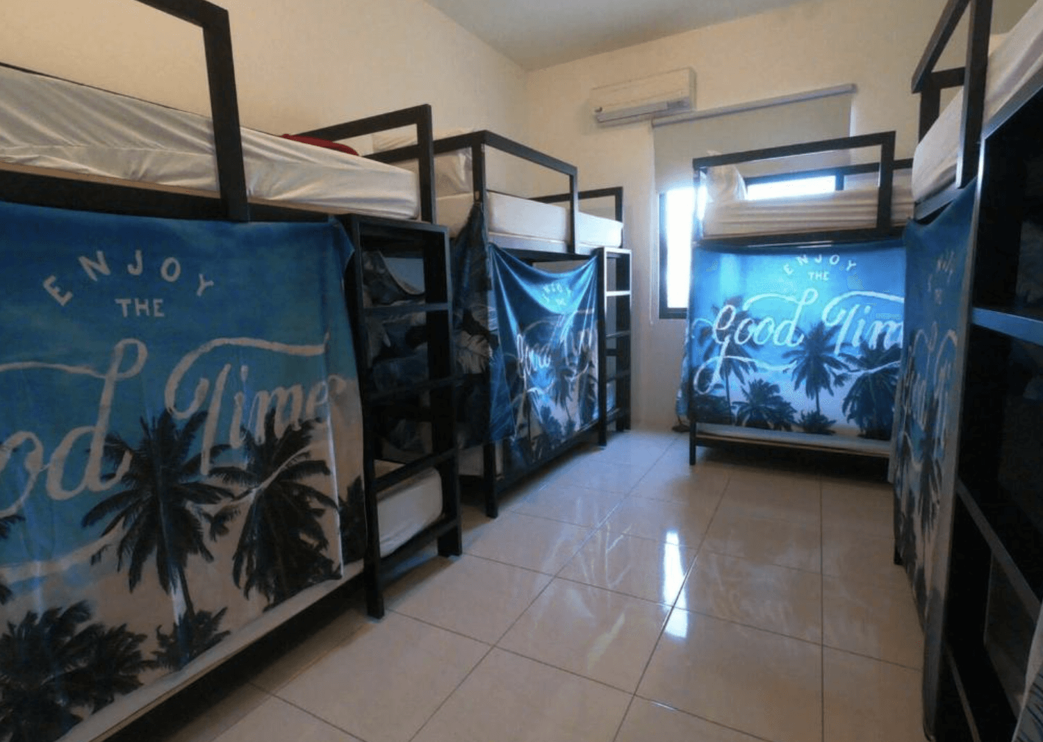 【東港住宿】留下旅舍的房間內設有多張上下舖，床邊以印有「Enjoy the Good Times」字樣與棕櫚樹圖案的布簾遮蔽，提供基本隱私，空間整潔並配有冷氣與窗戶。