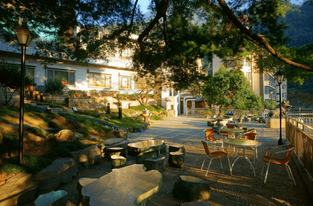 【谷關住宿】神木谷假期大飯店的戶外區擁有大片綠意與自然石材步道，擺放多組木桌椅與石椅，適合在清晨或午後享受陽光與山間微風。庭園周圍林木圍繞，燈光與造景點綴其間，環境清幽宜人，是散步與休憩的好地方。