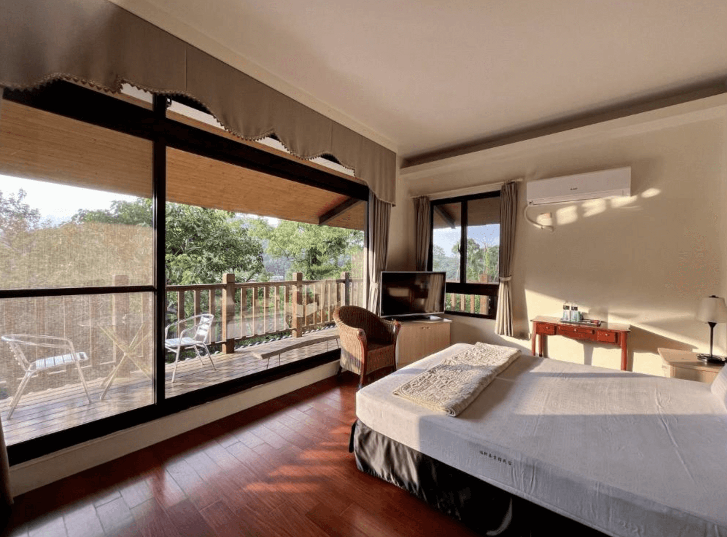 【三義住宿】福軒養生館民宿溫馨自然感雙人房，大片落地窗可眺望陽台與綠意景觀，房內設有電視、木質書桌與藤編椅，空間明亮通風。