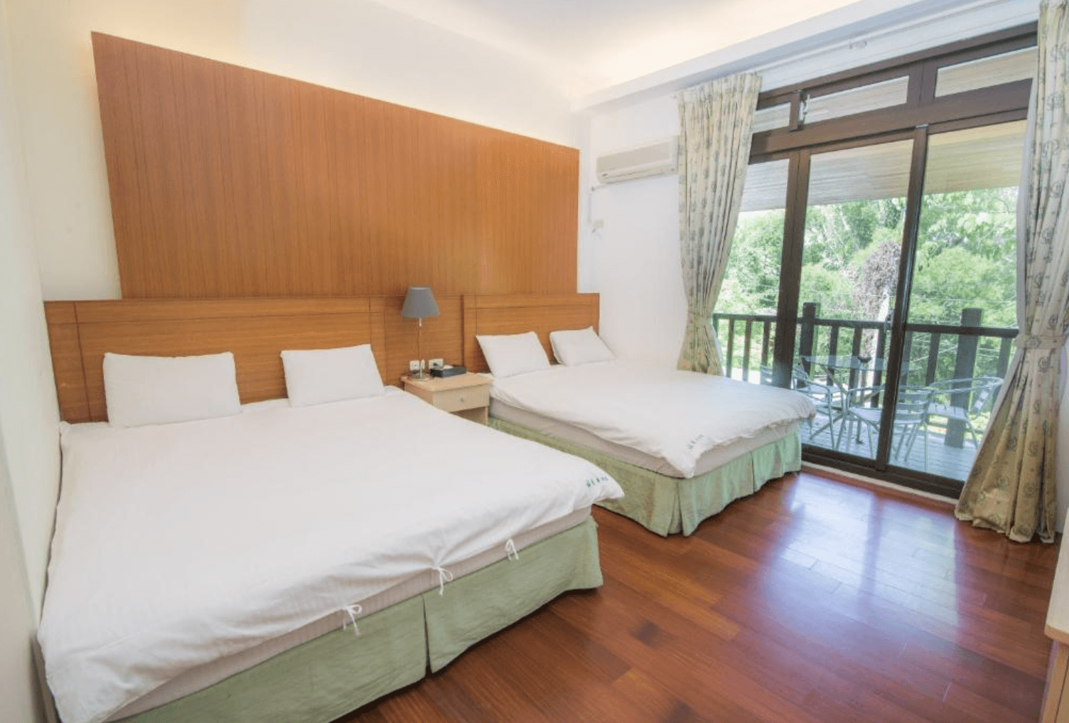 【三義住宿】福軒養生館民宿適合家庭入住的四人房，兩張雙人床並排設置，搭配木質地板與溫暖色調牆面，陽台外設有戶外休憩座椅與綠意景觀。