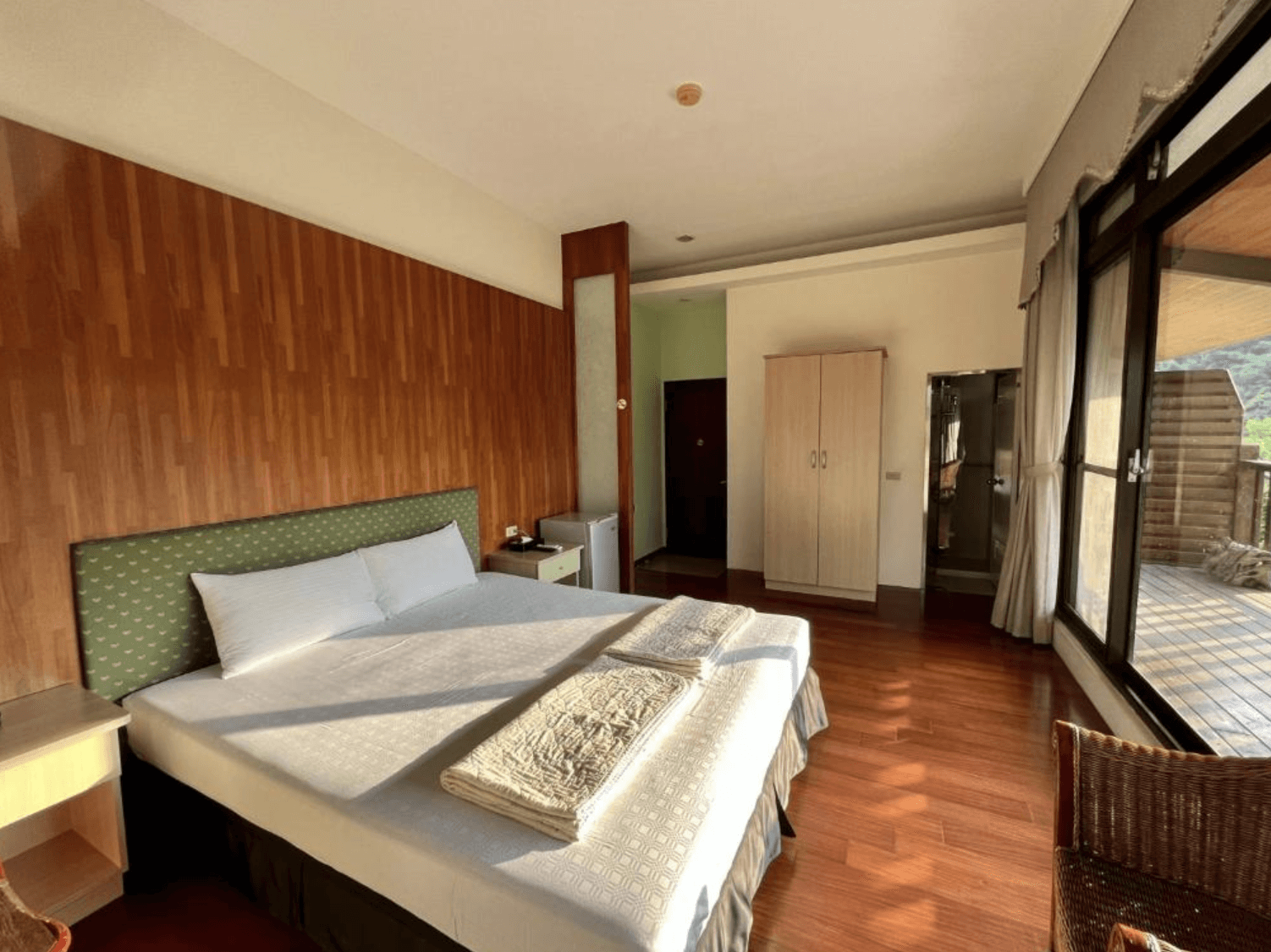 【三義住宿】福軒養生館民宿簡約舒適的雙人房設計，木質床頭牆搭配淺綠床頭板，設有衣櫃、小冰箱與乾濕分離浴室，窗邊陽台景致宜人。