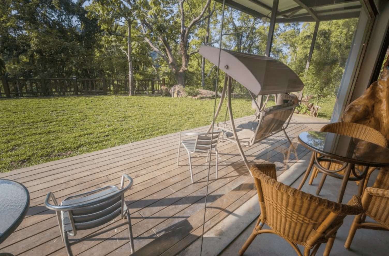 【三義住宿】福軒養生館民宿房間連接的戶外木平台設有吊椅、玻璃圓桌與藤編座椅，面對廣闊草地與林間景觀，是放鬆賞景的理想空間。