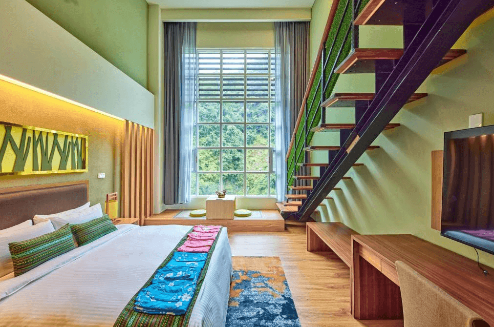 【谷關住宿】統一渡假村 谷關溫泉養生會館的設計風格，以嫩綠色牆面搭配溫潤木地板，大片玻璃窗外是綠意盎然的山景。房內配置一張大床與日式和式小茶几座位區，樓梯帶有人工草皮裝飾，兼具美觀與實用。