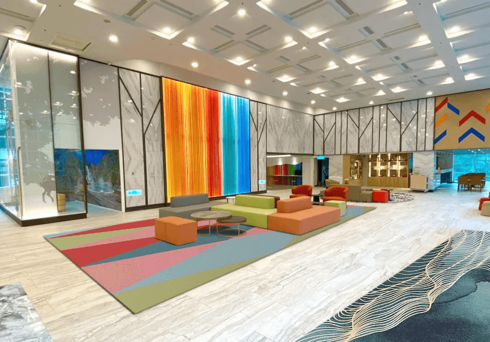 【谷關住宿】統一渡假村 谷關溫泉養生會館的大廳寬敞明亮，採現代幾何設計元素，牆面裝飾著亮眼的橘紅、藍綠色系燈光裝置，搭配色彩繽紛的沙發與地毯，營造出活潑且具藝術感的氛圍，是入住旅客的第一印象重點。