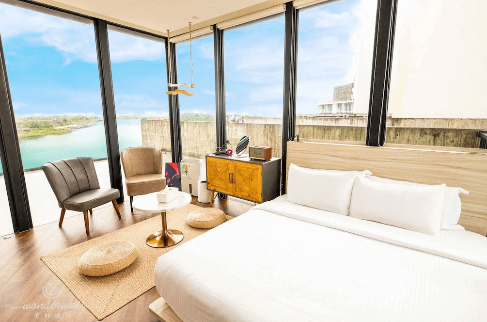 【五結住宿】美好境界民宿擁有大片玻璃窗的現代感臥室，配有雙人床、沙發椅與木質茶几，可欣賞河岸與藍天景致，空間寬敞明亮，設計簡約舒適。