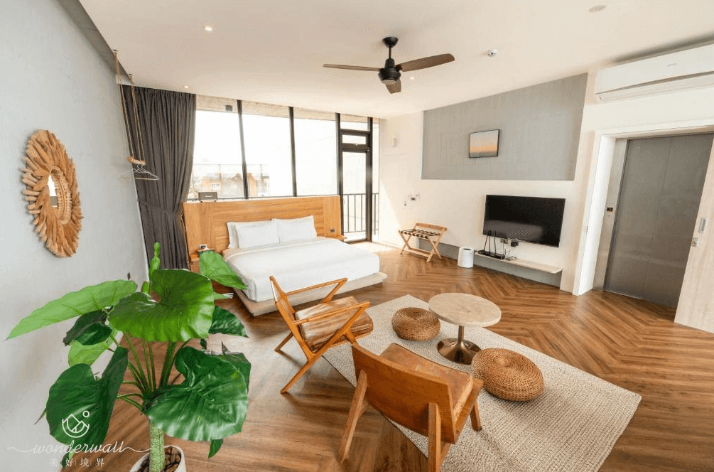 【五結住宿】美好境界民宿的室內空間開闊房型，配備雙人床、電視、休憩座椅與吊扇，大片落地窗引入自然光線，地板為溫潤木質拼接，設有綠色植栽增添生氣。