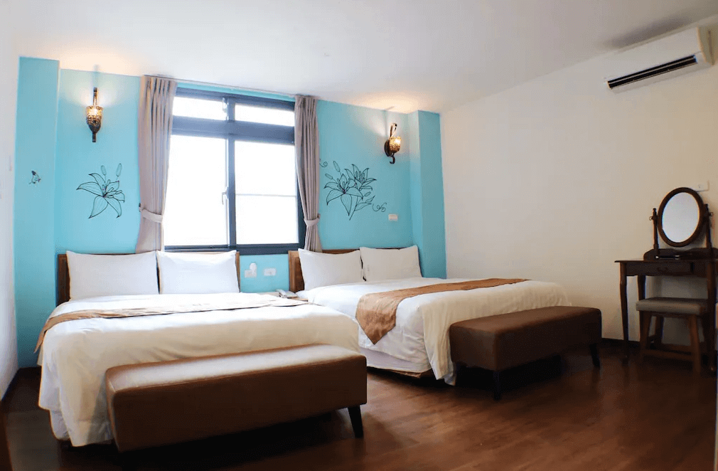 【關子嶺溫泉】“白河住宿”芳谷溫泉小棧採光良好的四人房，配有兩張雙人床，牆面繪有花卉壁畫，設有木質化妝台與冷氣，風格溫馨舒適。