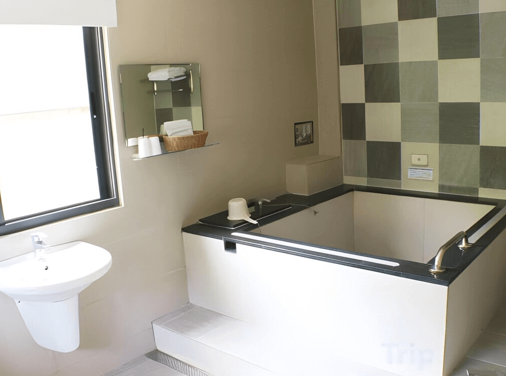 【關子嶺溫泉】“白河住宿”芳谷溫泉小棧的明亮浴室內設有方形泡湯池、洗手台與鏡子，牆面為黑白格紋磁磚設計，適合泡湯放鬆。