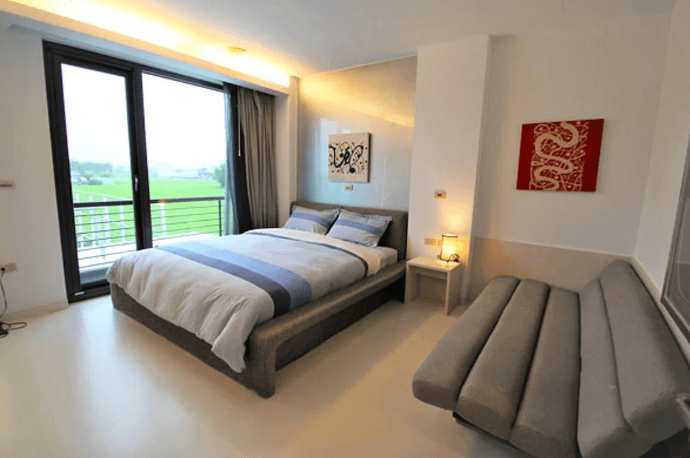【五結住宿】設計師的家休閒民宿俯瞰稻田美景的雙人房，房內設有灰色沙發床與藝術掛畫，白色牆面與明亮燈光打造清新簡潔的舒適氛圍。