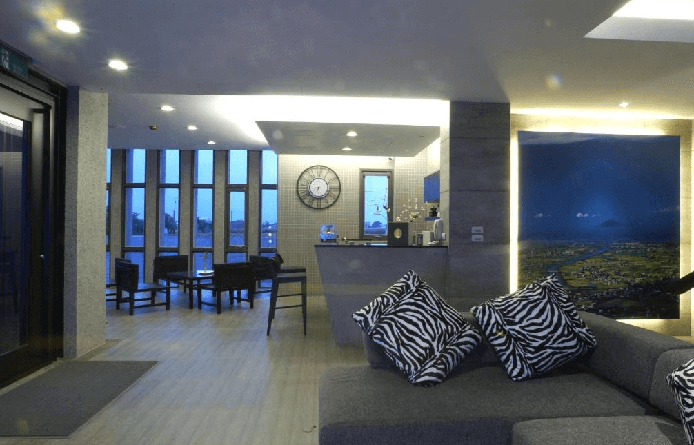 【五結住宿】設計師的家休閒民宿的接待大廳空間寬敞，設有多組沙發與座椅，搭配斑馬紋抱枕與現代感燈光設計，櫃檯後方為大片空拍攝影作品，營造舒適休憩氛圍。