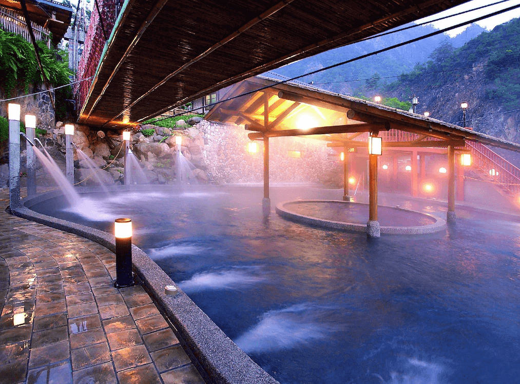 【谷關住宿】谷關 溫泉飯店的溫泉區以自然石材打造，設有多個池區與水療設備。夜間燈光點綴下更顯浪漫，木造涼亭與山景背景交織出溫暖療癒氛圍，適合在山林之間泡湯放鬆、洗去一身疲憊。