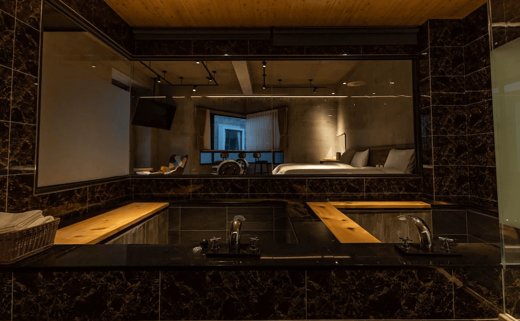 【蘇澳住宿】雙湯池衛浴空間設於貳十二度行旅房內，黑色大理石紋牆面與木質元素交織出高雅氛圍，大片玻璃隔間讓房內可俯視浴池空間。