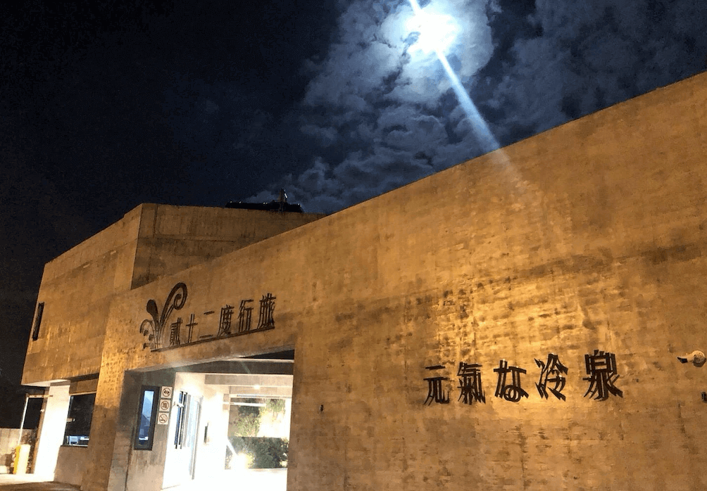 【蘇澳住宿】夜晚時分的貳十二度行旅外觀，混凝土建築風格搭配牆上「氯氛本冷泉」字樣，在月光與雲層映照下展現獨特的神秘氛圍。