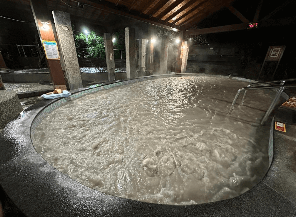 【關子嶺溫泉】關子嶺富野溫泉會館的夜間拍攝的戶外泥漿溫泉池，池水濃稠滾動，搭配木造屋簷與燈光照明，營造出濃厚溫泉療癒氛圍。