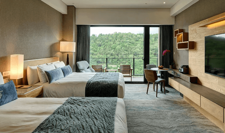 【台灣最貴飯店】雲品溫泉酒店的雙床房型，採木質元素與柔和燈光設計，設有陽台可眺望綠意盎然的森林景致，房內備有書桌與沙發椅，展現靜謐自然的度假氛圍。
