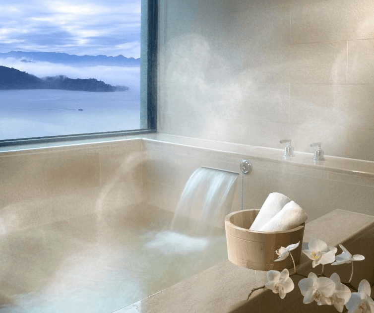 【台灣最貴飯店】雲品溫泉酒店的私人溫泉浴池設於靠窗位置，邊泡湯邊欣賞日月潭與雲霧山景，溫泉水流自然注入，營造療癒放鬆的泡湯體驗，旁有木桶與毛巾架等貼心備品。
