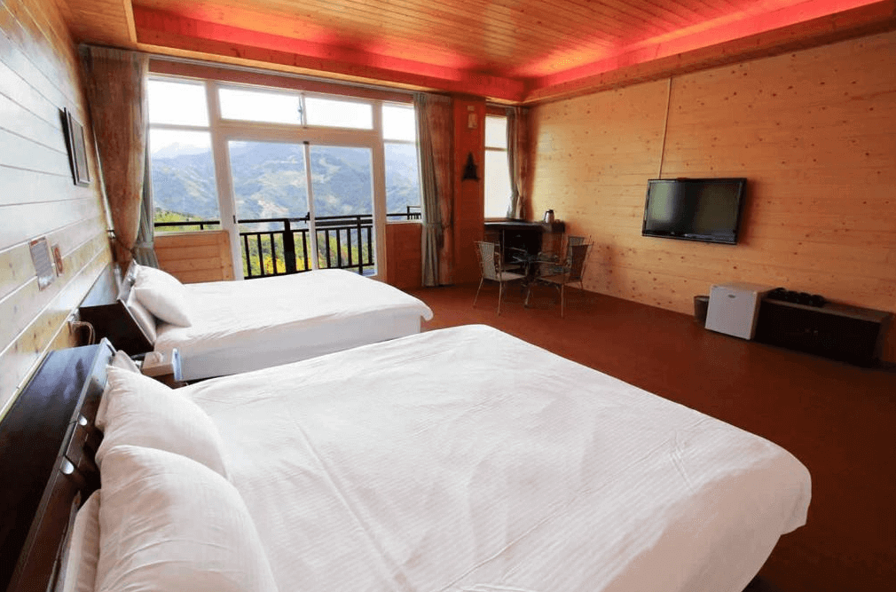 【清境農場住宿】雲濛仙境民宿的自然原木風格的四人房，設有兩張雙人床，木質牆面與天花板搭配隱藏式紅光氣氛燈，增添溫暖感，大片落地窗與陽台能欣賞壯麗山景，房內設有液晶電視、迷你冰箱與小型茶几，適合放鬆休憩。