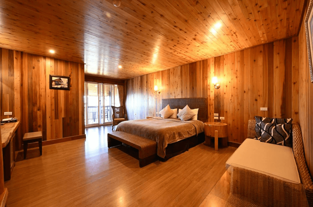 【清境農場住宿】雲頂渡假山莊以溫潤木質裝潢為主的雙人房，房內配有一張大床與長凳、沙發椅和書桌，整體氛圍溫馨典雅，後方落地窗外設有陽台，可遠眺景致。