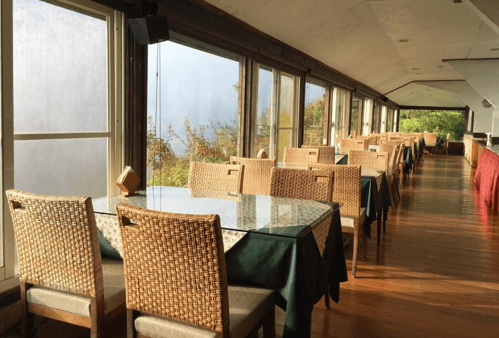 【清境農場住宿】雲頂渡假山莊採光明亮的景觀餐廳，擺放多張藤椅玻璃桌，窗外可眺望山林與遠方景色，空間寬敞通透，是享用早餐或晚餐的絕佳場域。