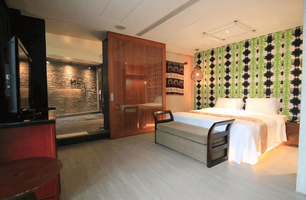 【谷關住宿】露泉渡假溫泉館的房內融合復古與現代元素，綠黑色幾何壁紙為整體空間增添活力，木質百葉拉門後方為大片石材牆泡湯區。床前設有長椅與吊燈，整體空間寬敞明亮，設計感十足。